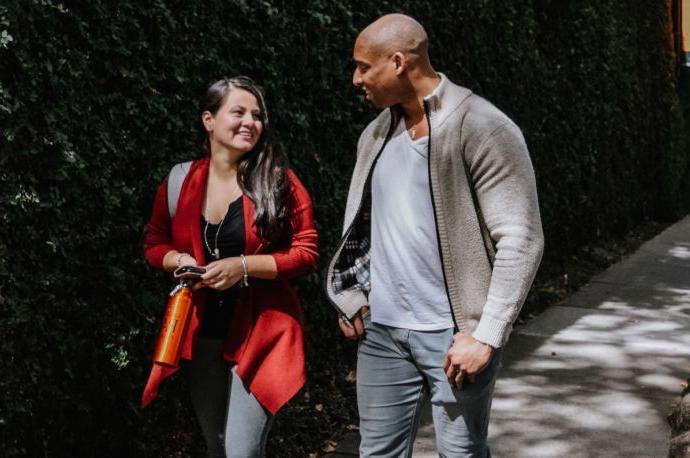 Photos shows two students walking together and smiling while looking at one another.