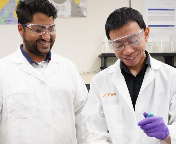 Two PCSP graduate students in a research lab wearing white coats 